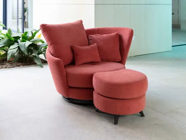 Fauteuil Roxane de Fama Sofás en revêtement rouge corail, au design arrondi, avec base pivotante et coussins décoratifs.