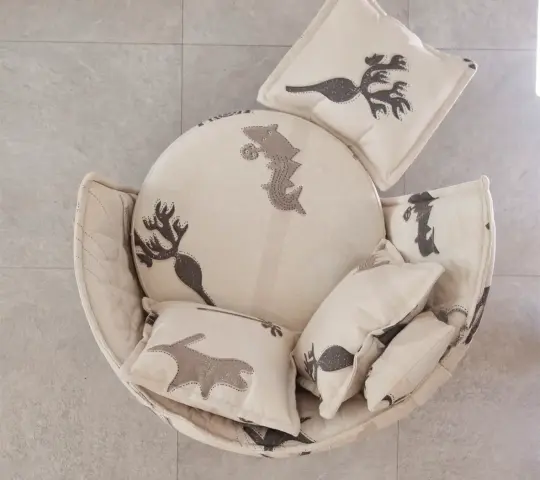 Top view of an armchair and footstool upholstered in Quetzal fabric, a light-coloured textile with decorative patterns in grey tones, accompanied by matching cushions.